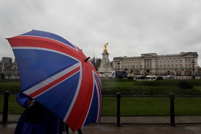 A cameraman protects himself from the rain with a Union flag umbreaal as he films Buckingham Palace in London, Wednesday, March 10, 2021. In countries with historic ties to Britain, allegations by Prince Harry and Meghan about racism within the royal family have raised questions about whether those nations want to be closely connected to Britain anymore after the couple's interview with Oprah Winfrey. (AP Photo/Kirsty Wigglesworth)