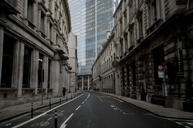 A person walks with an umbrella in light rain in the City of London financial district in London, Jan. 5, 2021, on the first morning of England entering a third national lockdown since the coronavirus outbreak began. British Prime Minister Boris Johnson on Monday night announced a tough new stay-at-home order, as authorities struggle to stem a surge in COVID-19 infections that threatens to overwhelm hospitals around the U.K. (AP Photo/Matt Dunham)