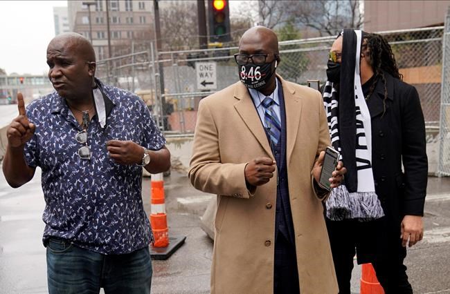 A family security personnel, left, talks to a reporter as Philonise Floyd, brother of George Floyd, listens as Floyd family members arrive at the Hennepin County Government Center, Friday, April 9, 2021, in Minneapolis where testimony continues in the trial of former Minneapolis police officer Derek Chauvin. Chauvin is charged with murder in the death of George Floyd during an arrest last May in Minneapolis. (AP Photo/Jim Mone)