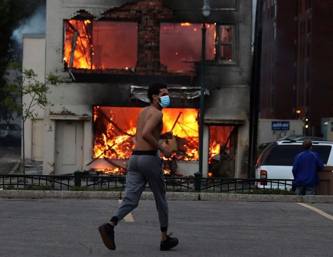 A man runs near a burning building after a night of unrest and protests in the death of George Floyd early Thursday, May 28, 2020 in downtown Minneapolis. Floyd died after being restrained by Minneapolis police officers on Memorial Day. A video taken by a bystander shows a Minneapolis police officer with his knee on the neck of a man in custody who later died. The four officers involved have been fired. (David Joles/Star Tribune via AP)