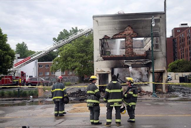 Firefighters stand as an aerial hose sends water on hot spots of a building destroyed near the Minneapolis Police Third Precinct Thursday, May 28, 2020, in Minneapolis, after a night of rioting and looting as protests continue over the death of George Floyd, who was seen on video gasping for breath during an arrest in which an officer kneeled on his neck. (AP Photo/Jim Mone)