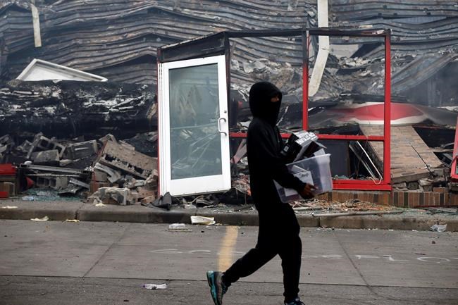 A man carries items past a burned out Auto Zone store near the Minneapolis Police Third Precinct Thursday, May 28, 2020, after a night of rioting and looting as protests continue over the death of George Floyd, who was seen on video gasping for breath during an arrest in which an officer kneeled on his neck. (AP Photo/Jim Mone)