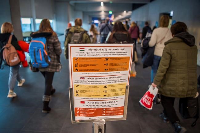 People pass by a notice as precautionary measures against the spreading of novel coronavirus, at Budapest Liszt Ferenc International Airport in Budapest, Hungary, Wednesday, Feb. 5, 2020. So far almost 900 passenger arriving directly from China have been examined at the airport. (Zoltan Balogh/MTI via AP)