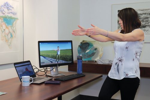 Employee Lea Currie tries a balance exercise that Manitoba Blue Cross wellness team lead Florent Thézard demonstrates on screen.