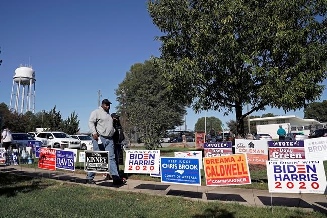 Voters walk past campaign signs at the Graham Civic Center polling location in Graham, N.C., Tuesday, Nov. 3, 2020. (AP Photo/Gerry Broome)