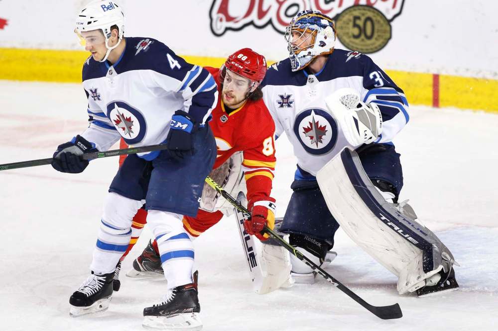 Larry MacDougal / The Canadian Press
Calgary’s Andrew Mangiapane, centre, battles between Jets goalie Connor Hellebuyck and Neal Pionk during the Jets 4-0 win Wednesday night in Calgary.