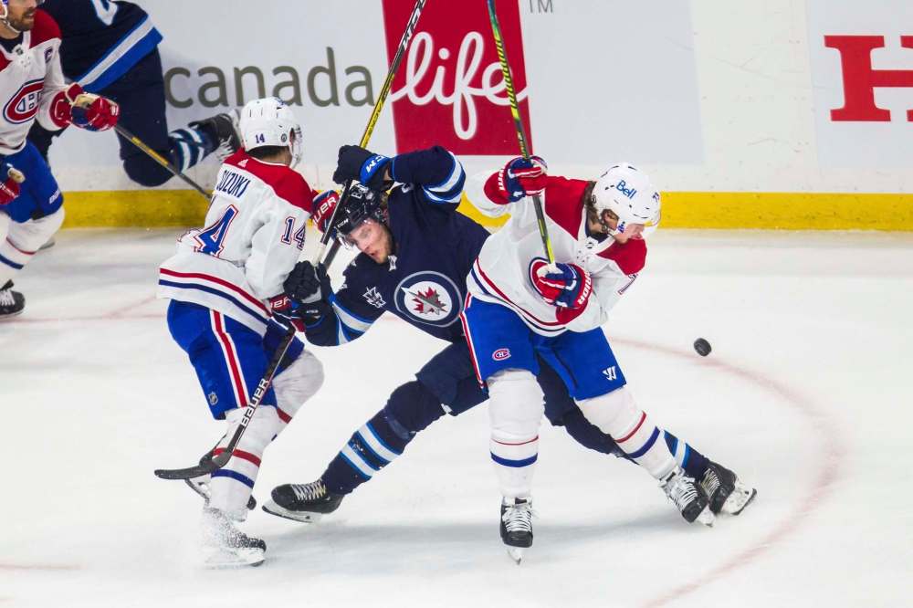 Montreal Canadiens forward Nick Suzuki (left), Winnipeg Jets’ Kristian Vesalainen and Canadiens forward Tyler Toffoli fight for the puck Friday. (Mikaela MacKenzie / WInnipeg Free Press)