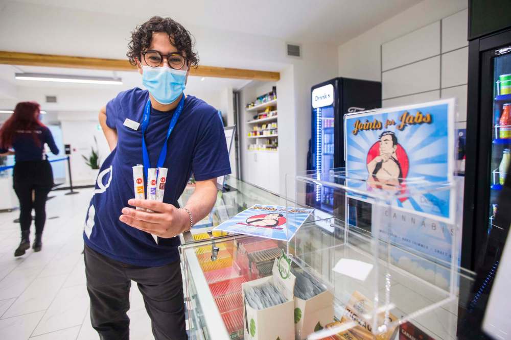 Cannabis specialist Adam El-Gabalawy holds a few joints in front of the entry box for the new Joints for Jabs pro-vaccination program at the Osborne Delta 9 Cannabis Store in Winnipeg. (Mikaela MacKenzie / Winnipeg Free Press)