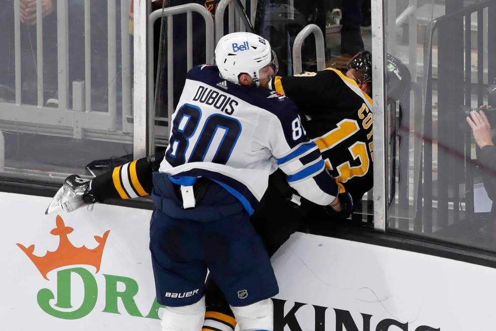 Winnipeg Jets’ Pierre-Luc Dubois checks Boston Bruins’ Charlie Coyle (13) and dislodges a section of plexiglass during the third period Saturday in Boston. (Michael Dwyer / The Associated Press)
