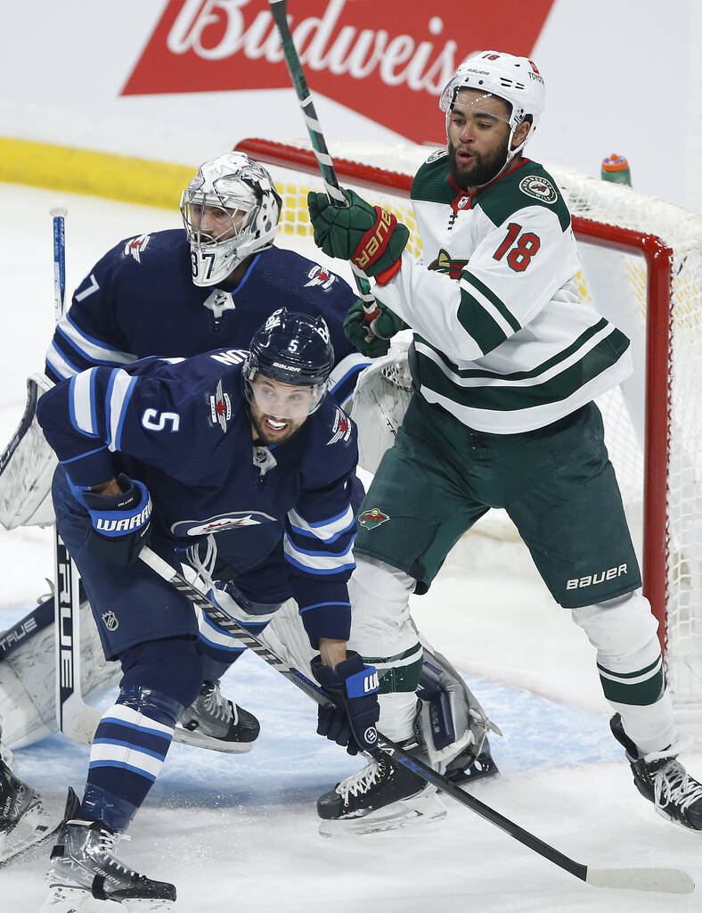 Winnipeg Jets' Brenden Dillon and Minnesota Wild's Jordan Greenway fight for position in front of Jets goaltender Connor Hellebuyck. THE CANADIAN PRESS/John Woods