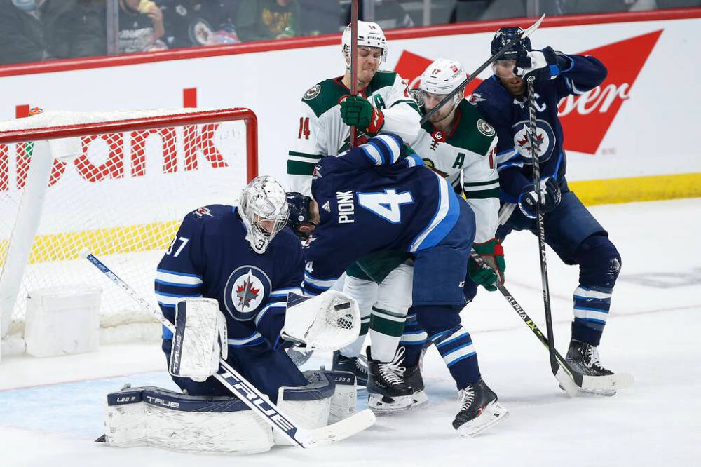 Winnipeg Jets goaltender Connor Hellebuyck saves the puck despite players crashing into him during the second period. THE CANADIAN PRESS/John Woods