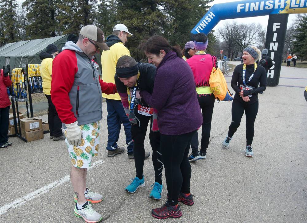 Jared Spier, who ran in honour of his partner, Joanne Schiewe, who died of brain cancer in 2016, is comforted by friends as he finishes the Winnipeg Police Service Half Marathon Sunday. (John Woods / Winnipeg Free Press)