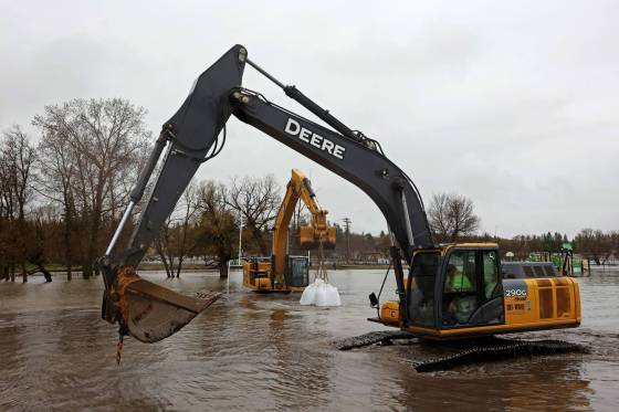 An excavator carries super sandbags through the rising floodwaters of the Little Saskatchewan River to create a dike to protect Minnedosa Collegiate. (Tim Smith / The Brandon Sun)