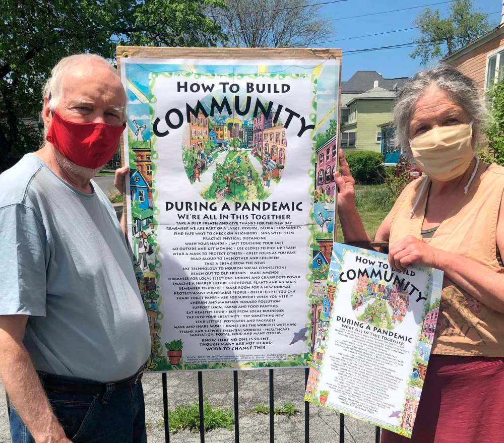Publisher Dik Cool (left) and art director Karen Kerney, with the new poster on pandemic measures to build community released in April by Syracuse Cultural Workers in Syracuse, N.Y. In New York State, people wearing masks are not required to stand two metres apart. (Kim McCoy / Syracuse Cultural Workers)
