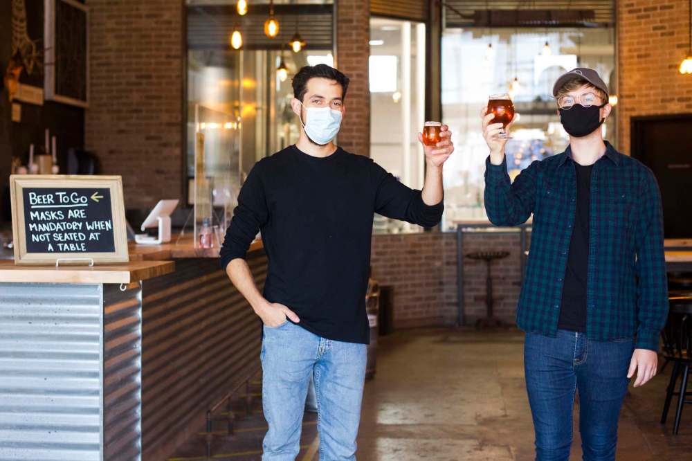 Taproom servers Brad Carrasco (left) and Dylan Huntly raise a glass at Barn Hammer. (Mikaela MacKenzie / Winnipeg Free Press)