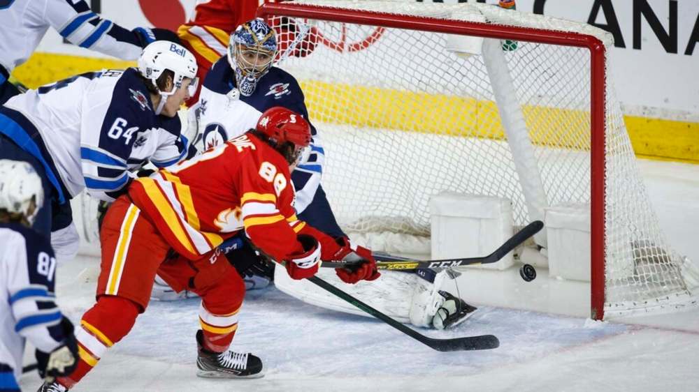 Winnipeg Jets goalie Connor Hellebuyck, centre, looks on as Calgary Flames' Andrew Mangiapane scores during the second period in Calgary, Tuesday. THE CANADIAN PRESS/Jeff McIntosh