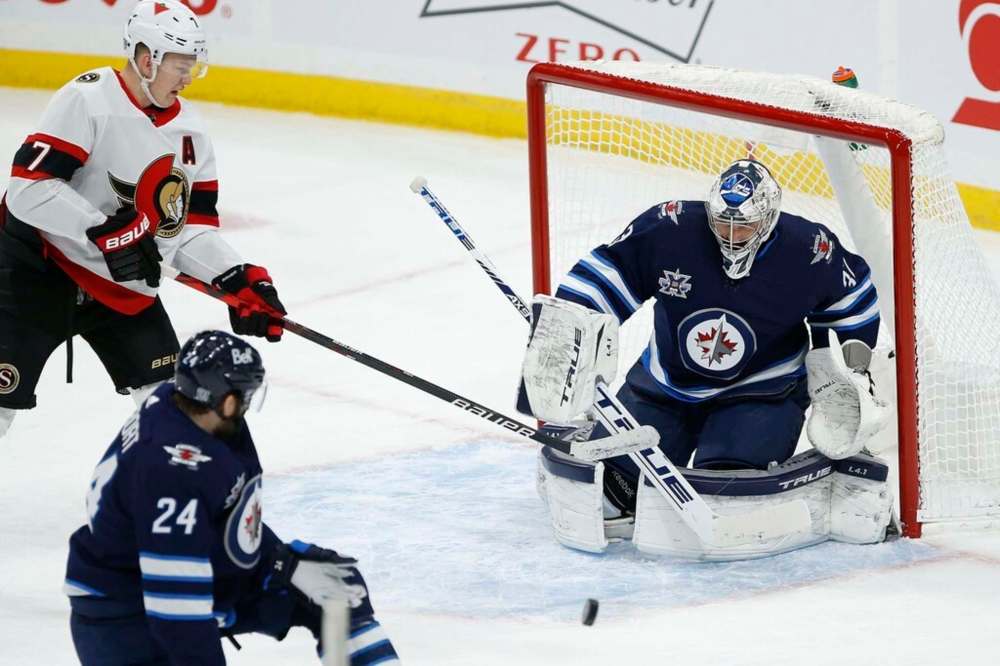 Winnipeg Jets' Derek Forbort (24) blocks the shot in front of goaltender Connor Hellebuyck (37) as Ottawa Senators' Brady Tkachuk (7) looks for a rebound during the first period in Winnipeg on Thursday. THE CANADIAN PRESS/John Woods