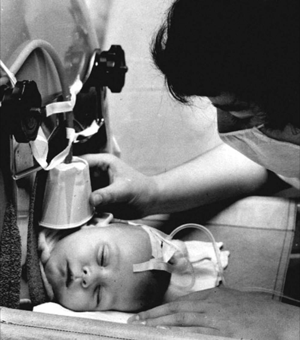 A nurse checks in on a young child hooked up to a respirator.