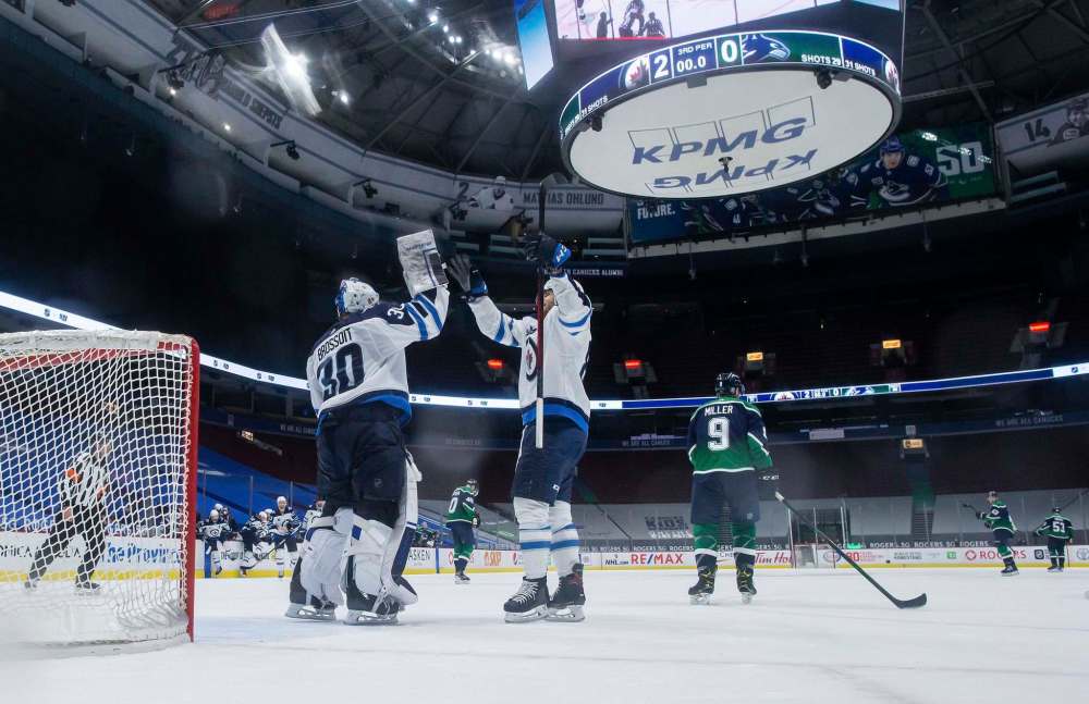 Winnipeg Jets goalie Laurent Brossoit (30) and Nathan Beaulieu celebrate after Winnipeg defeated the Vancouver Canucks 2-0 during an NHL hockey game in Vancouver, on Friday, February 19, 2021. (Darryl Dyck / The Canadian Press)