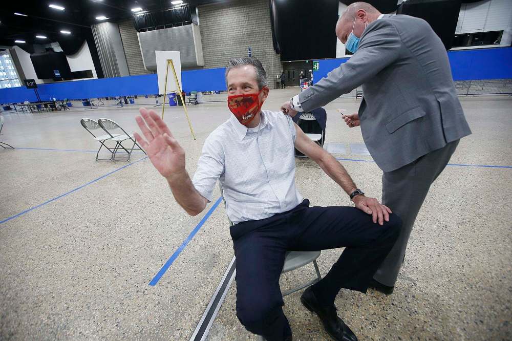 Manitoba Premier Brian Pallister waves to vaccination staff in Winnipeg’s convention centre as Dr. Brent Roussin, chief provincial public health officer, prepares to give him his COVID-19 vaccination Thursday. THE CANADIAN PRESS/John Woods