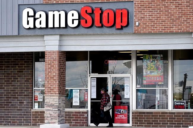 FILE - In this Oct. 15, 2020 file photo, a woman wears a face mask as she walks past a GameStop store in Des Plaines, Ill. Two hedge funds are bowing out of their short positions on the money-losing video game retailer. Citron Research’s Andrew Left said in a video posted on YouTube that his company is going to become more judicious in shorting stocks. Melvin Capital is also exiting GameStop, with manager Gabe Plotkin telling CNBC that the hedge fund was taking a significant loss. (AP Photo/Nam Y. Huh, File)
