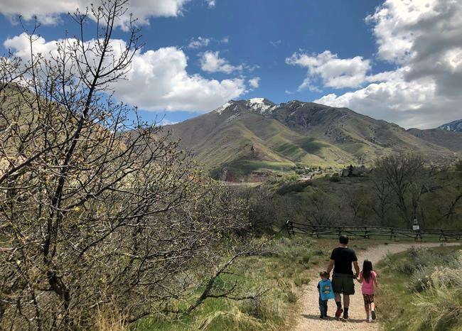 This April 22, 2020 image released by Lindsay Whitehurst, shows her husband Dave Watson walking with their two children, ages 3, left, and 5, on a trail in suburban Salt Lake City. When the coronavirus pandemic hit, Watson suddenly became a full-time dad. Outside “adventures” became the centerpieces of their days, giving him a front-row seat to the workings of their growing minds. (Lindsay Whitehurst via AP)