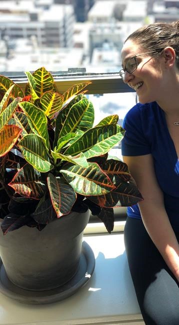This May 2019 photo shows Molly Sprayregen gazing at one of her new house plants in Chicago, Ill., which she named Dylan. (Meredith Bennett-Swanson/Molly Sprayregen via AP)