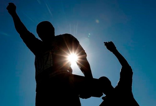 FILE - In this Oct. 17, 2018, file photo, a statue in honor of former Olympians Tommie Smith, left, and John Carlos is seen on the campus of San Jose State University in San Jose, Calif. Smith and Carlos raised their black-gloved fists while their national anthem played during the 200-meters medals ceremony at the Mexico City Olympics in 1968. Rule 50 of the IOC charter states: “No kind of demonstration or political, religious or racial propaganda is permitted in any Olympic sites, venues or other areas.” (AP Photo/Tony Avelar, File)