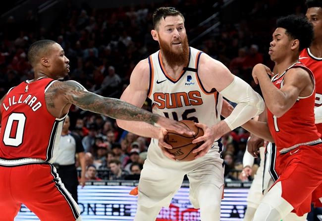 Phoenix Suns center Aron Baynes, center, drives to the basket between Portland Trail Blazers guards Damian Lillard, left, and Anfernee Simons, right, during the second half of an NBA basketball game in Portland, Ore., Tuesday, March 10, 2020. The Blazers won 121-105. (AP Photo/Steve Dykes)