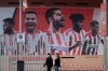 Two women wearing face masks pass by a giant poster of Atletico Madrid soccer players at the Wanda Metropolitano stadium in Madrid, Spain, Tuesday, May 5, 2020. The Spanish soccer league aims to restart in June without spectators. It's new compulsory protocols say all players, coaches and club employees must be tested for COVID-19 before training resumes, then regularly after that. All clubs' training facilities must be properly prepared and disinfected before players can start practising individually. (AP Photo/Paul White)