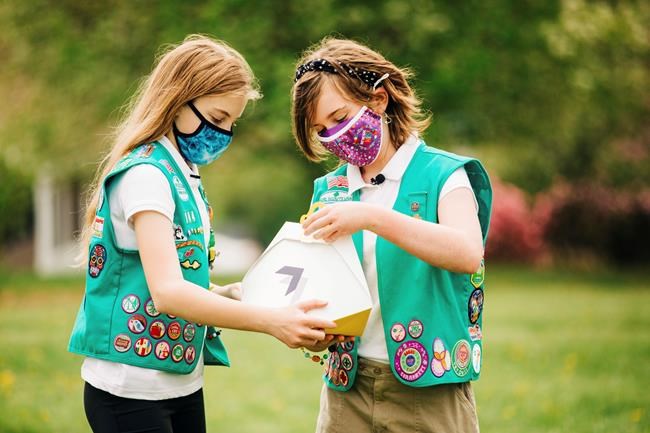 In this April 14, 2021 image provided by Wing LLC., Girl Scouts Alice Goerlich, left, and Gracie Walker pose with a Wing delivery drone container in Christiansburg, Va. The company is testing drone delivery of Girl Scout cookies in the area. (Sam Dean/ Wing LLC. via AP)