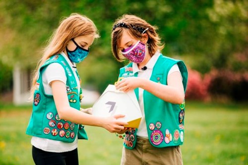 In this April 14, 2021 image provided by Wing LLC., Girl Scouts Alice Goerlich, left, and Gracie Walker pose with a Wing delivery drone container in Christiansburg, Va. The company is testing drone delivery of Girl Scout cookies in the area. (Sam Dean/ Wing LLC. via AP)