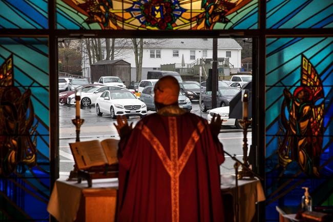 Rev. Peter Gower celebrates Mass from the front door of Our Lady of Grace Catholic Church as worshippers listen over the radio from their cars in the parking lot, Sunday, March 29, 2020, in Johnston, R.I. Gower started the Mass for those to attend from their cars last week as gatherings became restricted due to the coronavirus. The new coronavirus causes mild or moderate symptoms for most people, but for some, especially older adults and people with existing health problems, it can cause more severe illness or death. (AP Photo/David Goldman)