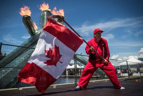 Ricky Johnson waves a Canadian flag on a hockey stick as the Olympic cauldron burns while attending Canada Day celebrations in Vancouver, on Monday July 1, 2019. A different kind of Canada Day is dawning this morning, with large celebrations in many parts of the country replaced with backyard barbecues and digital events. THE CANADIAN PRESS/Darryl Dyck