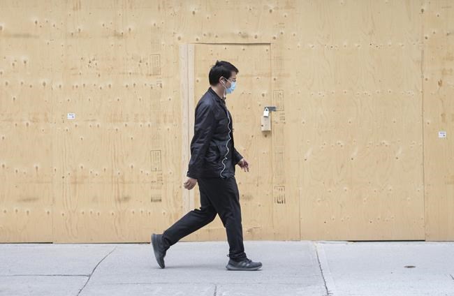 A man walks by a boarded-up storefront in Montreal, Sunday, May 3, 2020, as the COVID-19 pandemic continues in Canada and around the world. THE CANADIAN PRESS/Graham Hughes