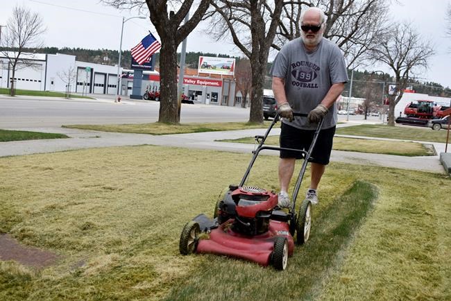 Tom Hagstrom mows the grass of St. Benedict's Catholic Church along Main Street in Roundup, Mont. on Monday, April 27, 2020. Most stores in the small town were considered essential businesses and stayed open despite a month-long closure order over the coronavirus that was lifted this week. (AP Photo/Matthew Brown)