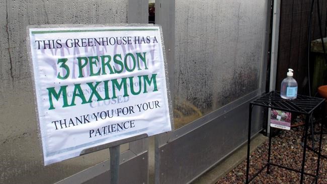 In this Monday, April 27, 2020, photo, with a bottle of hand sanitizer in the background, a sign limits the number of shoppers in the greenhouse of Evergreen Gardens of Vermont in Waterbury Center, Vt. Monday was the the first day businesses such as greenhouses and garden centers could allow a small number of customers inside as part of Vermont's gradual coronavirus pandemic reopening plan. (AP Photo/Wilson Ring)
