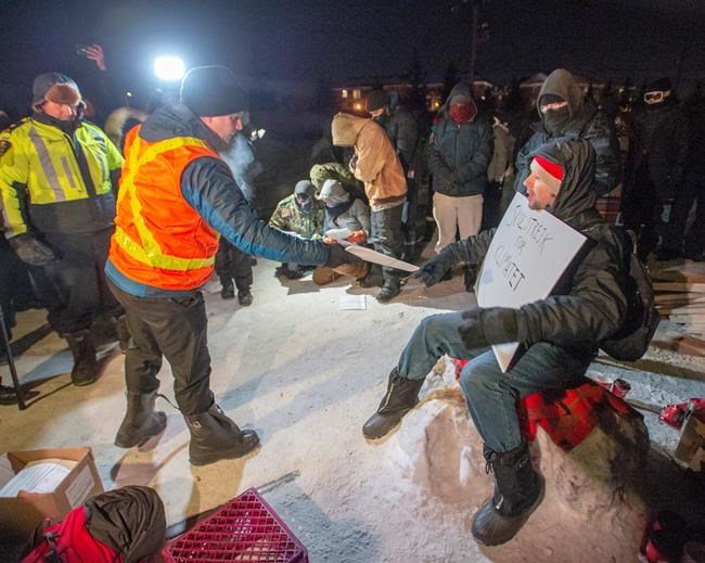 Police serve an injunction to protesters at a rail blockade in St-Lambert, south of Montreal, Que. on Thursday, February 20, 2020. The protesters are blocking the line in solidarity with the Wet'suwet'en hereditary chiefs opposed to the LNG pipeline in northern British Columbia. THE CANADIAN PRESS/Ryan Remiorz