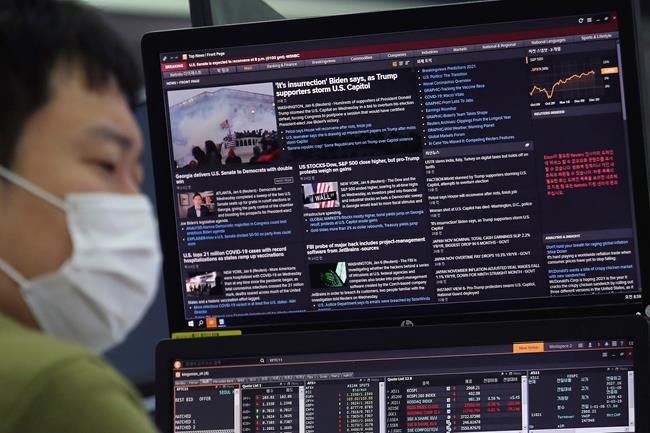 A currency trader works in front of a screen which shows a report on a mob by U.S. President Donald Trump supporters, at the foreign exchange dealing room of the KEB Hana Bank headquarters in Seoul, South Korea, Thursday, Jan. 7, 2021. (AP Photo/Ahn Young-joon)