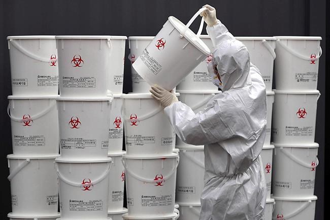 A worker in protective gear stacks plastic buckets containing medical waste from coronavirus patients at a medical center in Daegu, South Korea, Monday, Feb. 24, 2020. South Korea reported another large jump in new virus cases Monday a day after the the president called for