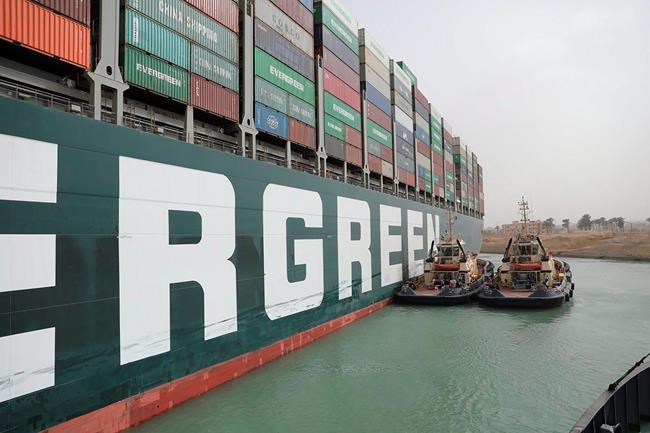 This photo released by the Suez Canal Authority on Thursday, March 25, 2021, shows two tugboats next to the Ever Given, a Panama-flagged cargo ship, after it become wedged across the Suez Canal and blocking traffic in the vital waterway from another vessel. An operation is underway to try to work free the ship, which further imperiled global shipping Thursday as at least 150 other vessels needing to pass through the crucial waterway idled waiting for the obstruction to clear. (Suez Canal Authority via AP)