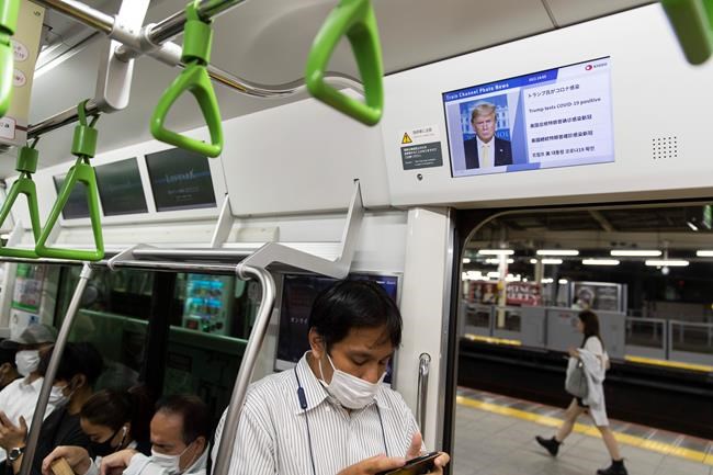 A train passenger plays a game on his cellphone under an onboard screen showing the news of U.S. President Donald Trump after he was tested positive for the coronavirus in Tokyo on Friday, Oct. 2, 2020. (AP Photo/Hiro Komae)