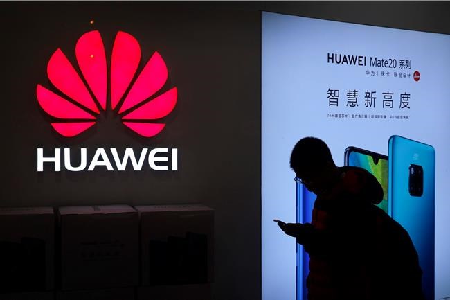 In this Dec. 11, 2018, photo, a man browses his smartphone outside a Huawei store at a shopping mall in Beijing. Chinese telecom giant Huawei Technologies says its sales rose about 18 percent in 2019 despite U.S. pressure to restrict its business. The estimate came Tuesday, Dec. 31, 2019 in an annual New Year's message to employees. The letter predicts a difficult year in 2020, saying that the U.S. (AP Photo/Andy Wong)