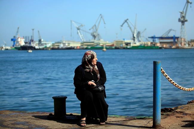 FILE - In this March 9, 2013, file photo, an Egyptian woman sits by the Suez Canal after several protesters set fire to tires on the city's dock in an attempt to prevent ships from coming in to the strategic city of Port Said at the Mediterranean end of the Suez Canal, in Egypt. A massive cargo ship has turned sideways in Egypt's Suez Canal, blocking traffic in a crucial East-West waterway for global shipping, according to satellite data accessed Wednesday, March 24, 2021. (AP Photo/Khalil Hamra, File)