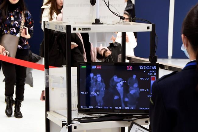 In this Jan. 16, 2020, photo, travelers from China's Wuhan go through body temperature scanners at Narita airport in Narita, near Tokyo. A fourth person has died in an outbreak of a new coronavirus in China, authorities said Tuesday, Jan. 21, 2020, as more places stepped up medical screening of travelers from the country as it enters its busiest travel period. (Kyodo News via AP)