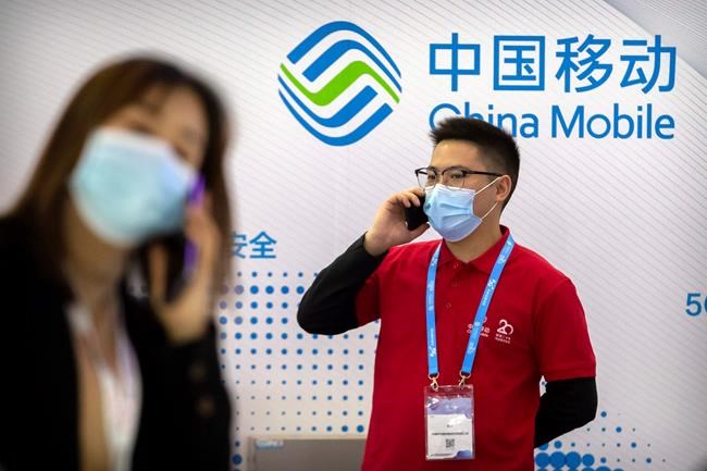 FILE - In this Oct. 14, 2020, file photo, people wearing face masks to protect against the spread of the coronavirus talk on their cellphones near a booth for Chinese telecommunications firm China Mobile at the PT Expo in Beijing. The New York Stock Exchange says it is withdrawing plans to remove shares of three Chinese state-owned phone carriers under an order by President Donald Trump.(AP Photo/Mark Schiefelbein, File)