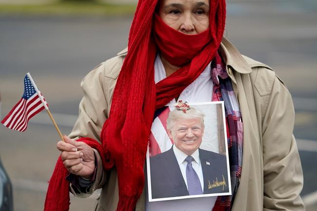 Tina Puente wears a portrait of President Donald Trump as she gathers with other supporters in anticipation of his visit to the U.S.-Mexico border, Tuesday, Jan. 12, 2021, in Harlingen, Texas. (AP Photo/Eric Gay)