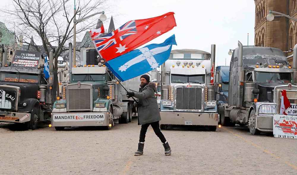 Nathan (Jacko) Jack, an Australian living in Toronto, waves flags in front of trucks that are parked in front of Parliament Hill as a rally against COVID-19 restrictions, which began as a cross-country convoy protesting a federal vaccine mandate for truckers, continues in Ottawa, on Monday, January 31, 2022. THE CANADIAN PRESS/ Patrick Doyle