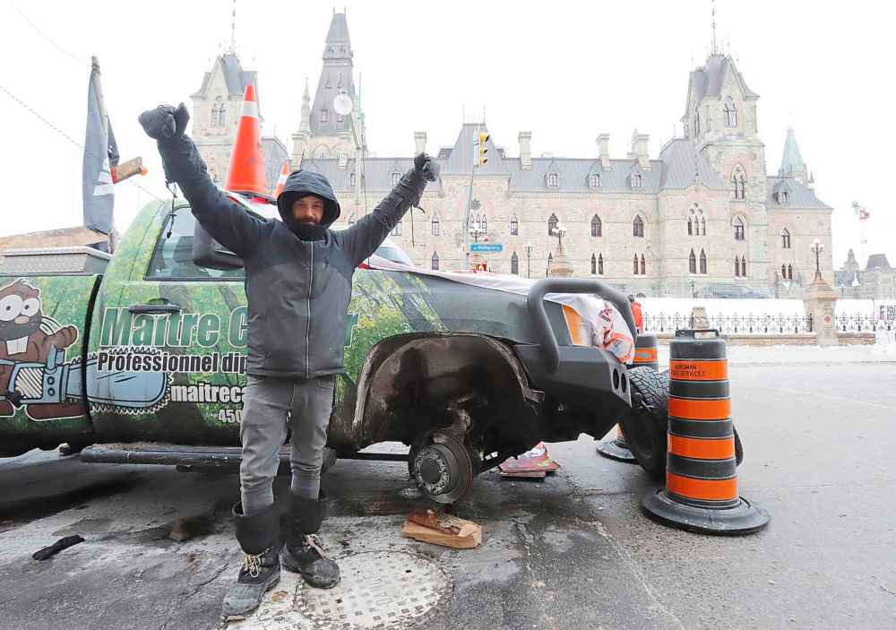 A man who removed the tires from his pickup truck stands in front of West Block on Parliament Hill as a rally against COVID-19 restrictions, which began as a cross-country convoy protesting a federal vaccine mandate for truckers, continues in Ottawa, on Monday, January 31, 2022. THE CANADIAN PRESS/ Patrick Doyle