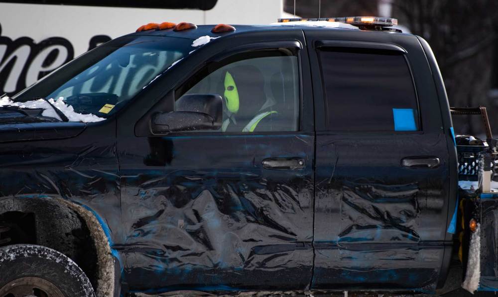 A tow operator wears a ski mask to protect their identity as they drive a tow truck with its company name concealed as they assist police in towing vehicles as they aim to end an ongoing protest against COVID-19 measures that has grown into a broader anti-government protest, on its 22nd day, in Ottawa, on Friday, Feb. 18, 2022. THE CANADIAN PRESS/Justin Tang